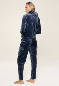 Ensemble de loungewear en velours bleu marine, comprenant un haut à capuche et un pantalon cargo avec poches latérales, texture lisse et coupe ajustée.