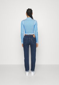 Ljusblå randig långärmad topp i kombination med mörka denimjeans. Jeansen har en klassisk femficksdesign, uppvikta fållar och en läderlapp.