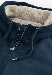 Námořnická modrá mikina na zip s texturovanou smetanově bílou sherpa podšívkou, nastavitelné šňůrky a stříbrným kovovým kováním pro zip.