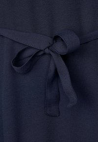 Mörkblått tyg med en jämn textur har en knytning i midjan som visar en slinga gjord av samma material.