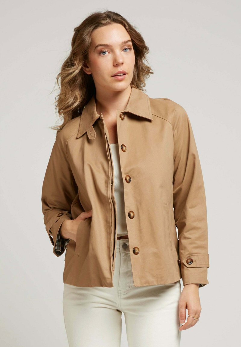 Veste marron clair en tissu lisse, dotée d'un col pointu, d'une fermeture avant à boutons et de longues manches avec détail aux poignets.