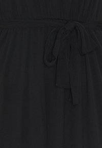 Tissu noir avec détail froncé et un nœud noué à la taille, suggérant une robe ou un vêtement.