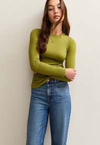 Olive green ribbed long-sleeve top with a crew neckline, paired with high-waisted blue denim jeans. Simple design, close-fitting silhouette.