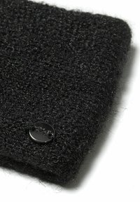 Tessuto di lana nero, testurizzato, con una superficie pelosa; presenta un accento di logo in metallo nero nell'angolo. Forma rettangolare, morbido e spesso.