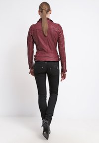 Bordeauxrode leren jas met een getailleerd ontwerp, gestructureerde schouders en asymmetrische accenten. Draagt zwarte skinny jeans en enkellaarsjes.