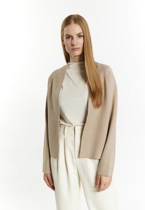 Beige cardigan met open voorkant, lange mouwen en zachte textuur, gelaagd over een crème top met hoge hals, gecombineerd met witte op maat gemaakte broeken.