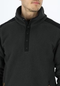 Pullover in pile grigio scuro con collo alto, apertura con bottoni e dettagli neri sulle spalle. Tessuto morbido e vestibilità casual.
