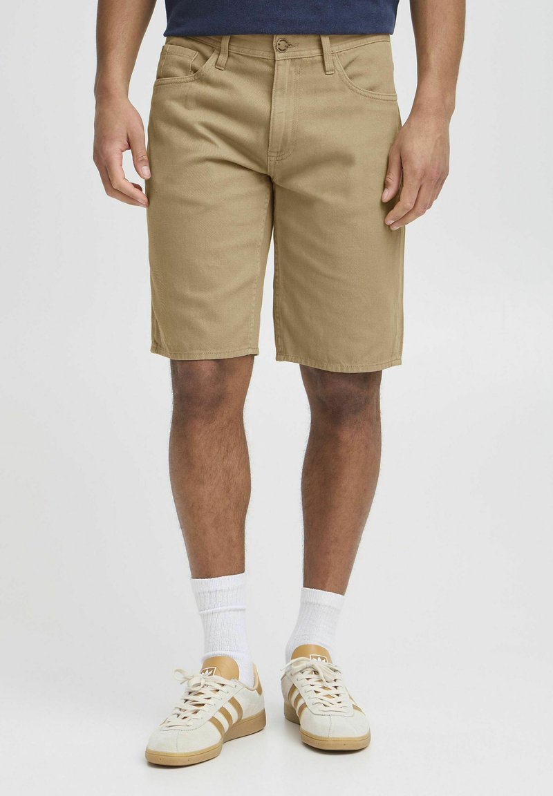 Shorts kaki en mélange de coton. Présentent une coupe droite, des passants de ceinture et cinq poches. Portés avec une chemise marine et des chaussettes blanches.