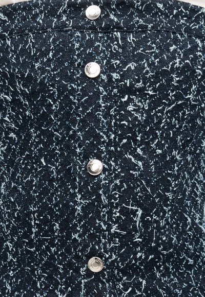 Tissu en denim bleu foncé avec des fibres duveteuses blanches dispersées, présentant quatre boutons-pression métalliques argentés alignés verticalement.