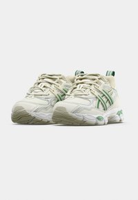 Sportovní boty světlé smetanové barvy se zelenými akcenty, vrchní část z texturované kůže a síťoviny, zavazování na tkaničky a měkká podrážka. Gumová podrážka s protiskluzovým vzorem.