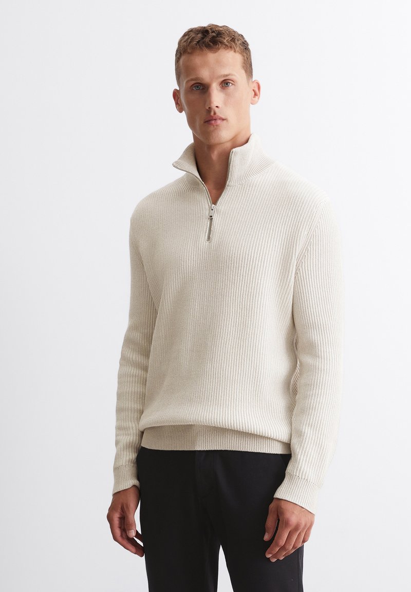 Cremfarbener, gerippter Pullover mit halbem Reißverschluss und hohem Kragen. Der Stoff hat eine weiche Textur, ist mit langen Ärmeln und einer lockeren Passform gestaltet.