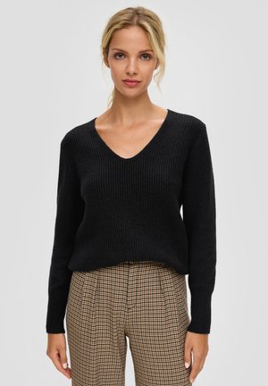 Zwarte geribbelde trui met een diepe V-hals en lange mouwen, gecombineerd met bruine geruite high-waisted broek. Zachte textuur en een comfortabele pasvorm.