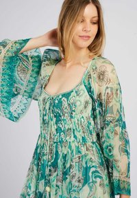 Robe à imprimé floral dans des tons de vert avec un corsage smocké et des manches cloche fluides et transparentes. Présente des accents en perles le long des bords des manches et du col.