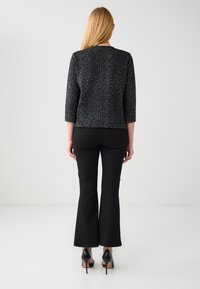 Haut à imprimé léopard noir avec manches trois-quarts, associé à un pantalon évasé noir et des escarpins noirs, vu de dos.