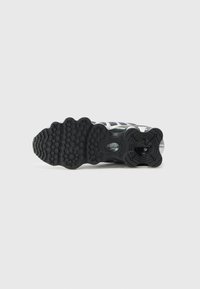 Sneaker with a textured black rubber sole, featuring a wave design and visible air cushioning. Color accents include silver and navy blue.