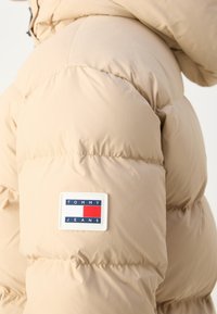 Manche de doudoune beige avec un patch logo rectangulaire Tommy Jeans aux couleurs bleu, blanc et rouge.