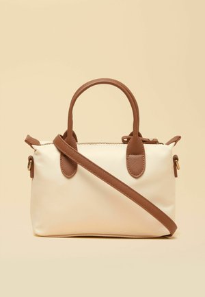 Borsa rettangolare color crema con manici in pelle marrone, tracolla staccabile e cerniera superiore su sfondo beige.