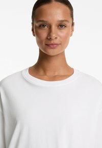 Top alb cu mânecă lungă, cu o croială lejeră, decolteu rotund și o textură moale și netedă. Design simplu, fără modele sau embellismente.