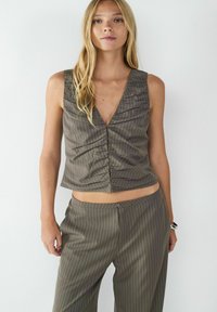 Olivengroen cropped top met verticale witte strepen, met een diepe V-hals en geplooide details aan de voorkant. Complementaire broeken.