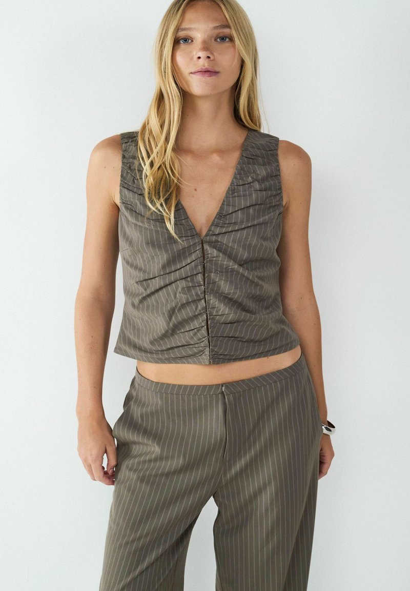 Olivengroen cropped top met verticale witte strepen, met een diepe V-hals en geplooide details aan de voorkant. Complementaire broeken.