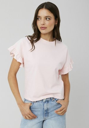 T-shirt rose clair à manches courtes avec des poignets à volants, col rond, coupe décontractée, porté avec un jean en denim bleu taille haute. Texture de tissu lisse.