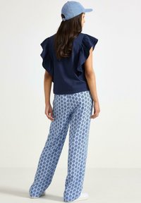 Top blu navy con maniche a volant, abbinato a pantaloni a gamba larga azzurro chiaro con motivi a rombi. Il modello indossa un cappello di denim.
