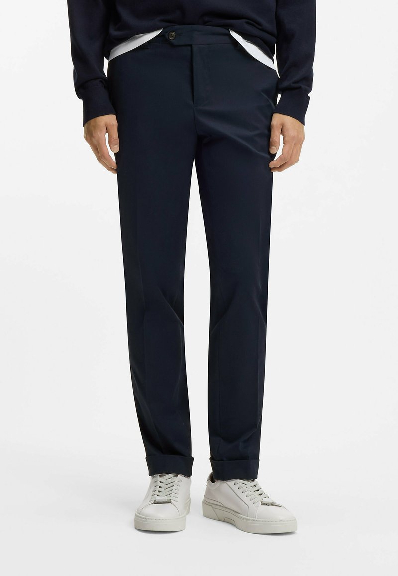 Pantalon bleu marine en tissu lisse, avec un devant plat, des poches latérales et des ourlets retroussés, assorti à des baskets blanches.