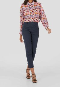 Vaaleanpunainen ja monivärinen kukkakuosiset nappipaita, jossa on pitkät, puffatut hihat, yhdistettynä tummansinisiin kapeisiin housuihin ja mustiin remmisandaaleihin.