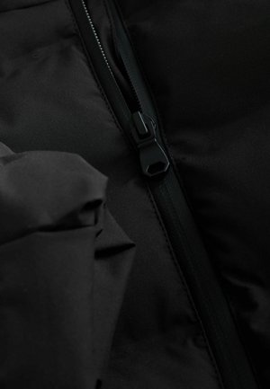 Schwarzer gepolsterter Jackenstoff mit sichtbarem Reißverschluss. Das Material wirkt glatt und matt, mit einem eleganten, minimalistischen Design und verdeckten Nähten.