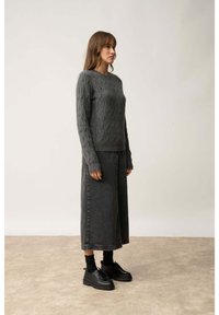 Szary sweter z grubej dzianiny z długimi rękawami, w połączeniu z szerokimi czarnymi dżinsowymi culottes i czarnymi sznurowanymi butami. Jednolity kolor, teksturowany materiał.