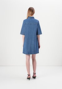 Jeanskjole i blått med korte ermer, krage og rett silhuett. Har synlig søm og en lett utsvingt kant.