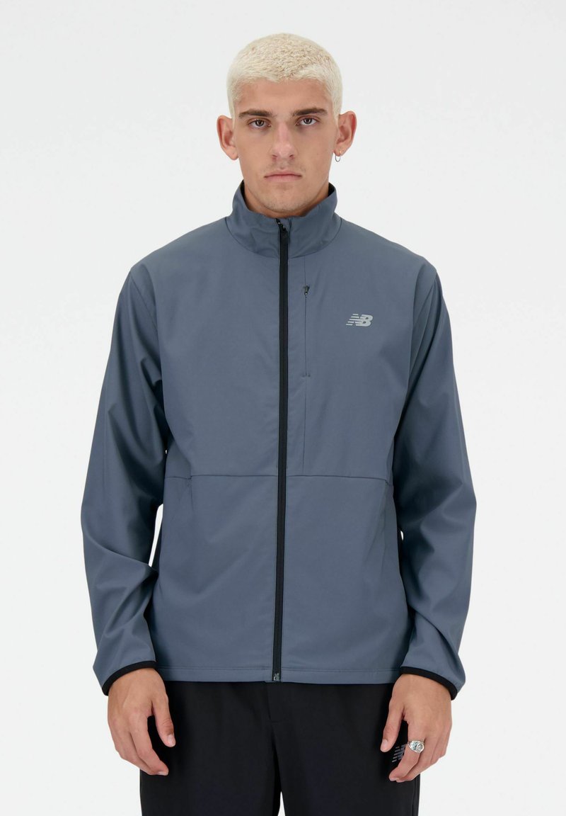 Chaqueta ligera gris con un cuello alto, cierre de cremallera completo y detalle de logo en el pecho izquierdo. Cuenta con una textura suave y puños elásticos.
