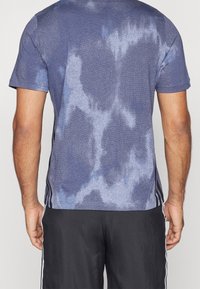 Mörkblå sportt-shirt med texturerat mönster, korta ärmar och svarta sidosträck. Tillverkad av ventilerande tyg för aktiv användning.