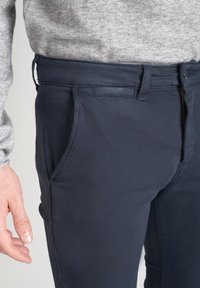 Pantaloni blu navy con una texture liscia, tasche laterali e chiusura con zip. Il tessuto sembra leggero e aderente in vita.