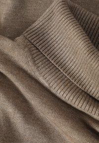 Gros plan d'une manche pliée d'un pull en maille côtelée marron montrant la texture détaillée du tissu et les coutures.