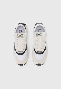 Beige and white athletic shoes featuring mesh and suede materials, black accents, padded tongue, and a logo on the tongue and side.