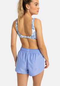 Blauer Sport-BH mit Floralprint und Rundrücken, kombiniert mit hellblauen Shorts mit elastischem Bund, die einen lockeren Schnitt und Saumdetails aufweisen.