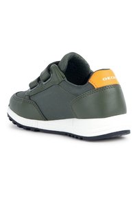 Baskets vertes avec une tige texturée, des bandes Velcro, et un accent orange contrastant au talon. Elles présentent une semelle intermédiaire blanche et une semelle extérieure noire.