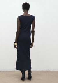 Abito lungo senza maniche di colore blu navy, con scollatura rotonda, silhouette aderente e texture liscia, abbinato a stivaletti neri con tacco all'altezza della caviglia.
