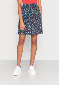 Jupe à imprimé floral marine avec des fleurs rouges et bleues, taille élastique, coupe droite évasée, associée à des baskets blanches.