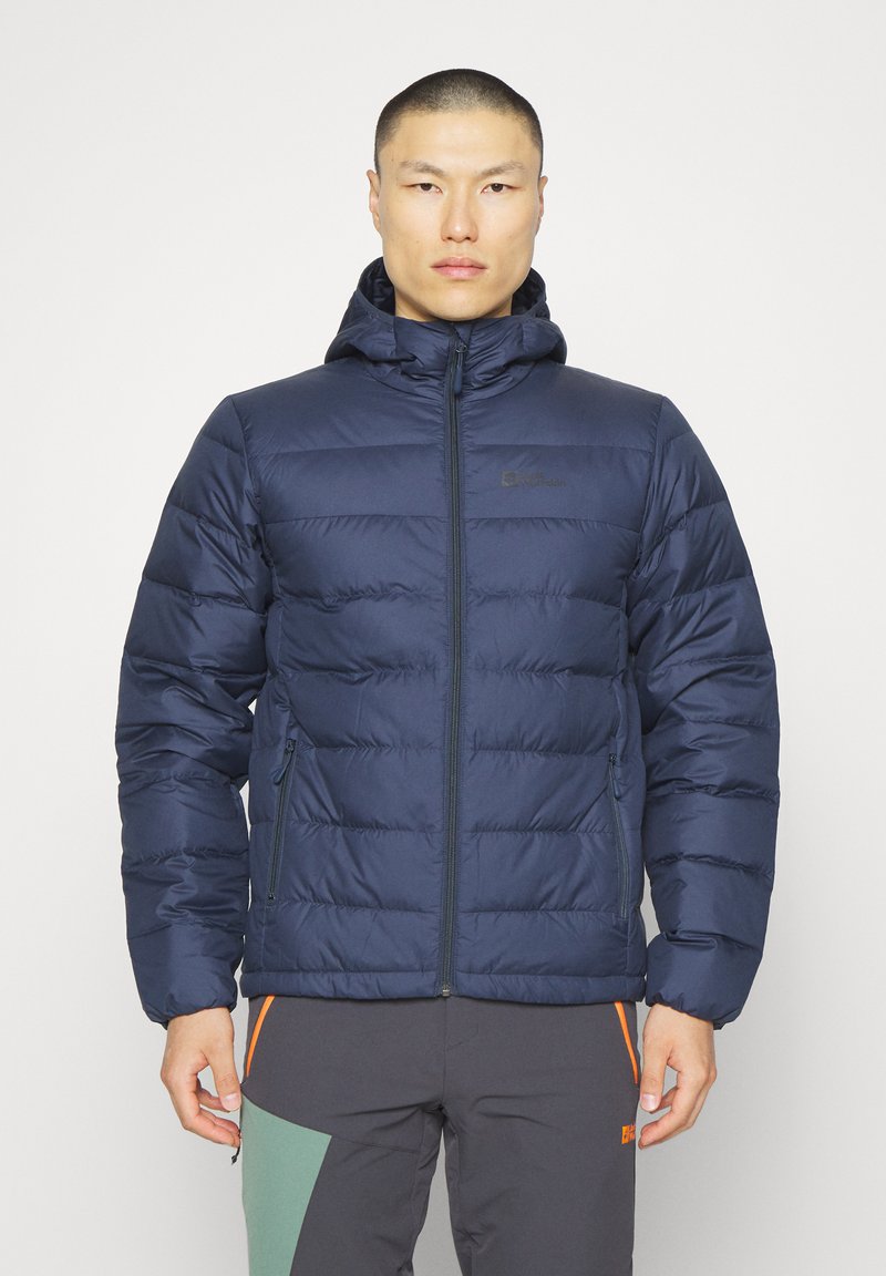 Giacca imbottita blu navy con cappuccio e chiusura con zip, caratterizzata da una texture trapuntata e un logo sul petto sinistro. Tessuto resistente con polsini elastici.
