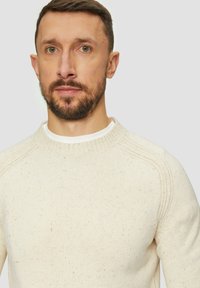 Kremowy sweter dzianinowy z teksturowanym wzorem i ściągaczem przy szyi, o klasycznym kroju oraz raglanowymi rękawami.