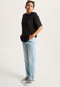 Camiseta de algodón negra con un corte relajado, jeans de mezclilla azul claro con corte recto y zapatos de tela a rayas en blanco y negro.