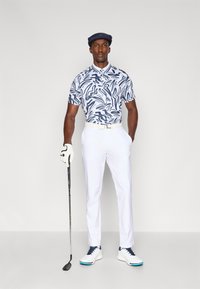 Conjunto de golfe com uma polo de padrão abstrato azul e branco, calças brancas, um boné escuro, sapatos de golfe brancos com detalhes azuis e uma luva.