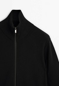 Maglione nero con zip e colletto alto, texture a coste e dettaglio della zip argentata sul davanti, con spalle scese.