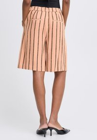 Shorts en lin couleur pêche avec des rayures verticales marron, taille élastique et deux poches arrière, offrant une coupe ample et décontractée.