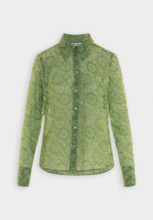 Camisa verde de manga larga con botones, confeccionada en tela transparente con estampado floral y cuello puntiagudo, exhibida sobre un fondo claro.