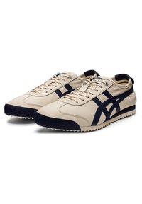 Beige leather sneakers featuring navy accents and three stripes on the sides. Rounded toe and textured rubber outsole for grip.