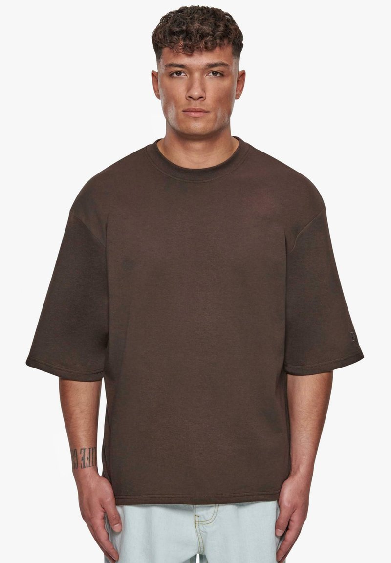 Hnědý oversize tričko s krátkým rukávem, vyrobené z měkké bavlněné látky, s kulatým výstřihem a jemnými švy.