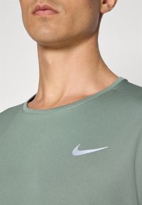 T-shirt Nike vert avec un col rond, un tissu texturé et un petit logo en argent sur la partie gauche de la poitrine.